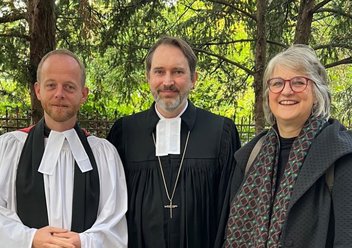 Reverend Jack Noble, Pfarrer Roland Wicher und Pfarrerin Barbara Hustedt stehen vor der Kirche in Mariendorf