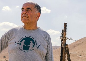 Elie Avidor von den Combatants for Peace, ein älterer Mann, steht in einer Wüstenlandschaft. Er trägt ein graues T-Shirt mit dem Logo der Organisation. 