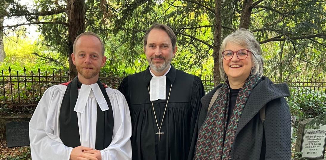 Reverend Jack Noble, Pfarrer Roland Wicher und Pfarrerin Barbara Hustedt stehen vor der Kirche in Mariendorf